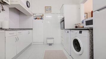 A compact kitchen with white cabinets, a built-in washing machine, and a small trash bin.