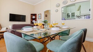 A dining area with a glass table, teal chairs, and a breakfast setting with orange juice glasses.