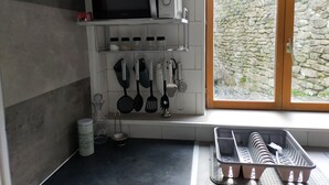 Una cucina con forno a microonde, utensili, macchina del caffè e vista su un muro in pietra attraverso una finestra.