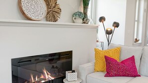 Una sala de estar moderna con chimenea, un sofá con cojines decorativos y una mesita auxiliar.