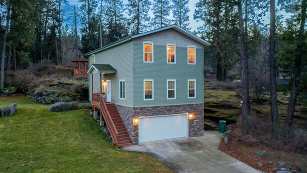A two-story house with a stone foundation, a front porch, and a garage. - Rocky Ridge Retreat | Cozy Post Falls Home (Post Falls)