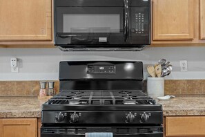Une cuisine équipée d’un micro-ondes noir, d’une cuisinière à quatre brûleurs et d’une horloge numérique affichant 4 h 17.