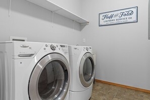 Un espace dédié à la blanchisserie, équipé de deux sèche-linge Whirlpool à chargement frontal, et d’une enseigne indiquant « Fluff and Fold Laundry Service Co. ».
