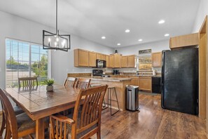 A modern kitchen with wooden cabinets, a black refrigerator, and a dining area with a wooden table and chairs.