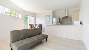 A modern kitchen with a grey sofa, a dining area with chairs, and a view of the outdoors. - Cosy Modern Home close to Fremantle (Coolbellup)