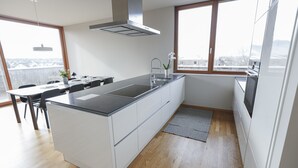 A modern kitchen with a central island, a built-in oven, and a window providing a view of the city. - 100 m2 Penthouse mit 3 Schlafzimmer, Grosser Überdachter Terrasse und Bergblick (Klaus)