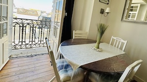 A balcony with a view of buildings, a table with a white tablecloth, and a chair.