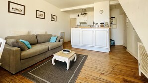 A living room with a sofa, a coffee table, and a kitchen area with cabinets and a clock.