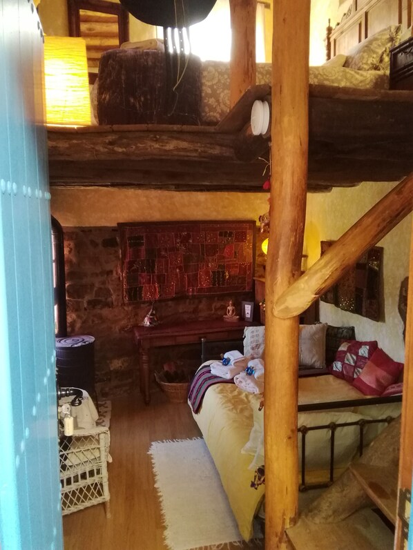 Quarto rústico com beliche, uma mesinha com luminária e parede de pedra.