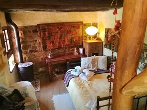 Um quarto rústico com parede de pedra, uma cama com cabeceira de madeira, uma pequena escrivaninha com abajur e um objeto pendurado na parede.