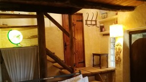 A rustic room with a bed, a wooden staircase, a small table, and a wall-mounted lamp. - Shillong House by Eco Moyano Posada (Gaucin)
