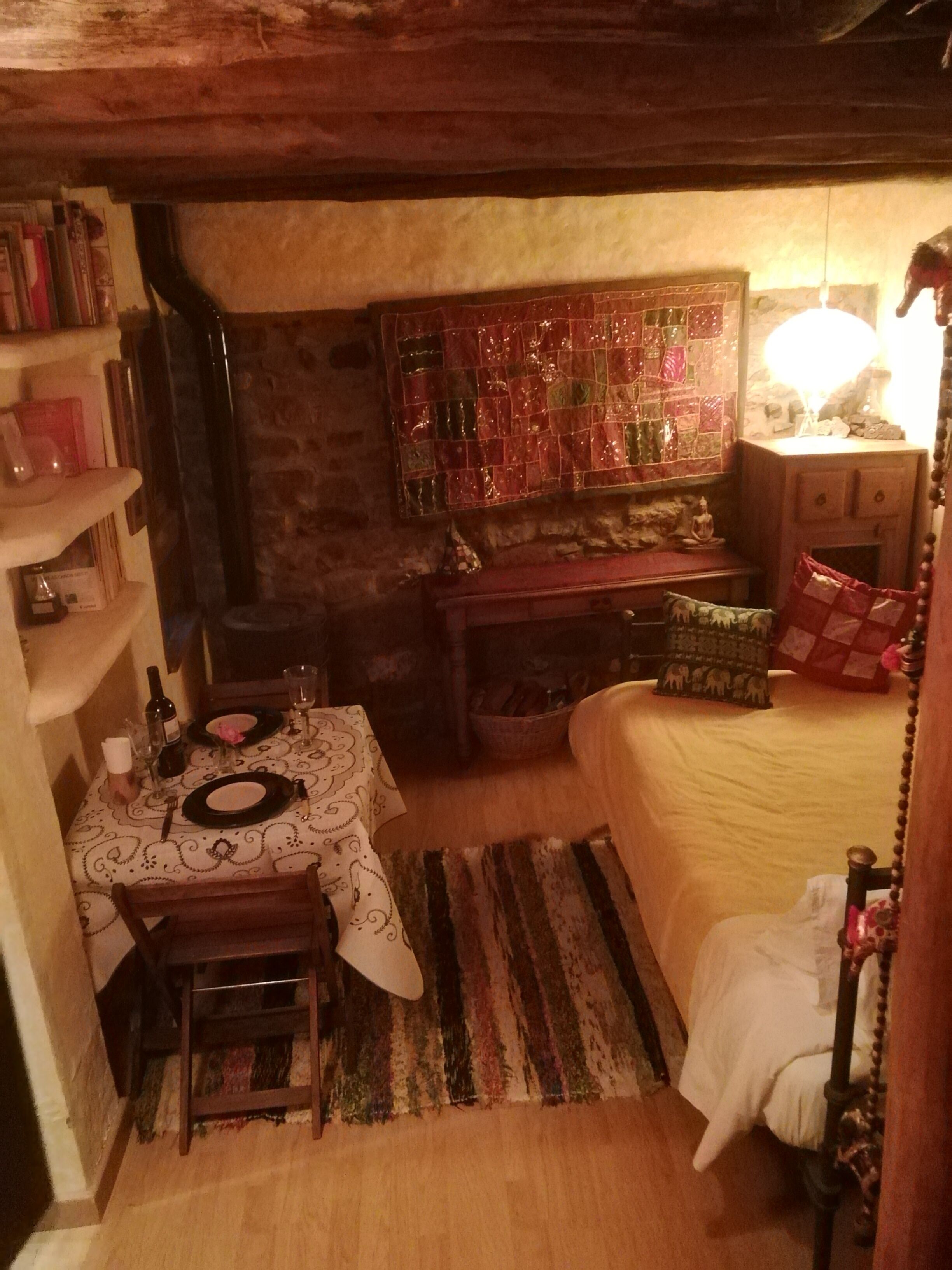 Ein gemütliches Zimmer mit einem Bett, einem für zwei Personen gedecktem Tisch, einem Bücherregal und einer dekorativen Steppdecke.