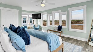A bedroom with a bed, a ceiling fan, a TV, and large windows with a view of the outdoors. - Otter Space | Waterfront | Dog Friendly | Hot Tub (Surf City)