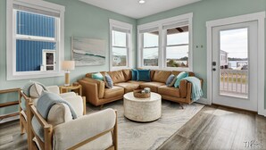 A spacious living room with a large L-shaped sectional sofa, a round coffee table, and a view of the outside through large windows. - Otter Space | Waterfront | Dog Friendly | Hot Tub (Surf City)