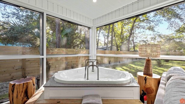 Een moderne badkamer met een vrijstaand bad, grote ramen en uitzicht op een tuin.
