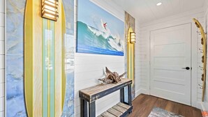Een hal met strandkunst van een surfboard, een houten console tafel met een zeester, en een deur met een gouden handgreep.
