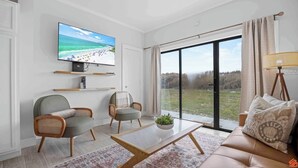 A modern living room with a large TV, comfortable seating, and a view of the outdoors. - Sandy Toes Studio: Your Beachfront Getaway Awaits (Fort Walton Beach)