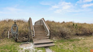 Una scala di legno che conduce a un accesso alla spiaggia, con un tubo e un lampione nelle vicinanze.