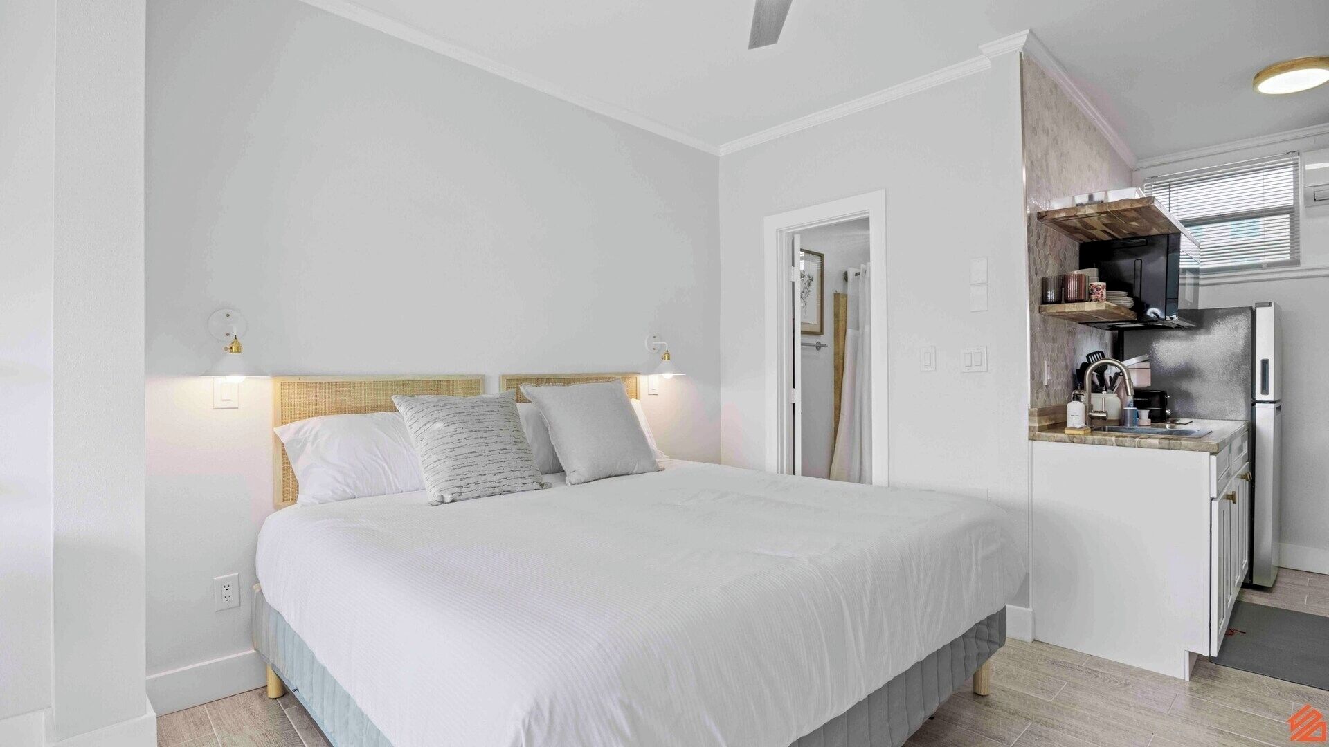 A bedroom with a bed, bedside lamps, and a kitchenette with a refrigerator and stove.