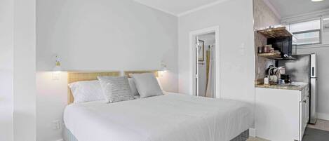A bedroom with a bed, bedside lamps, and a kitchenette with a refrigerator and stove.