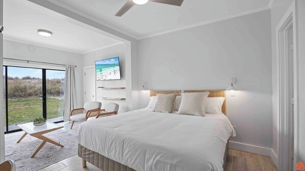 A modern bedroom with a large bed, a TV mounted on the wall, and a view of the outdoors through a glass door.