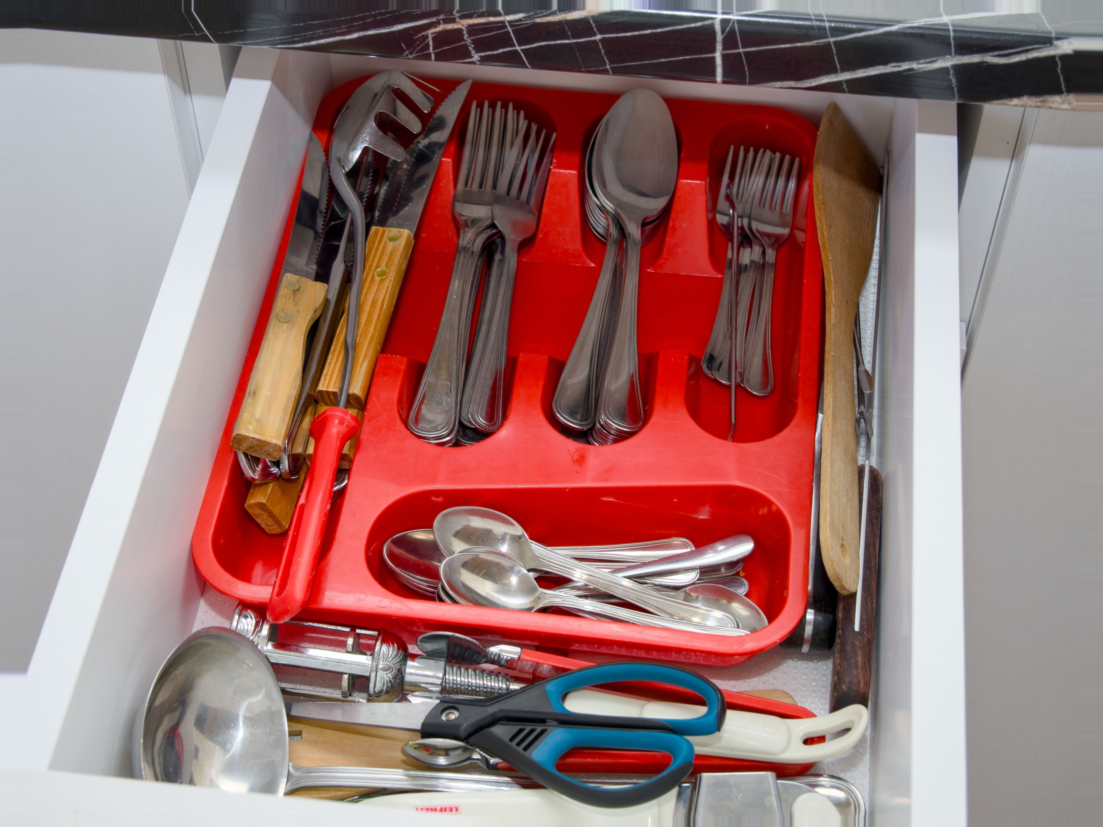 A drawer containing various kitchen utensils and tools, including forks, spoons, and a pair of scissors.