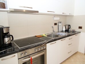 A modern kitchen with a black stovetop, white cabinets, a stainless steel sink, and a coffee maker. - 5 minutes from the beach spacious apartment for families and group of friends (Durrës)