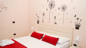 A hotel room with a bed, red and white bedding, a nightstand with a lamp, and wall decorations.