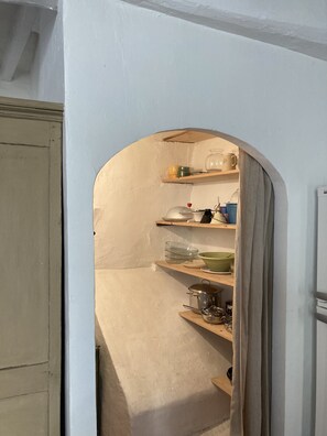 A narrow kitchen with white walls, a wooden door, and shelves holding kitchenware.