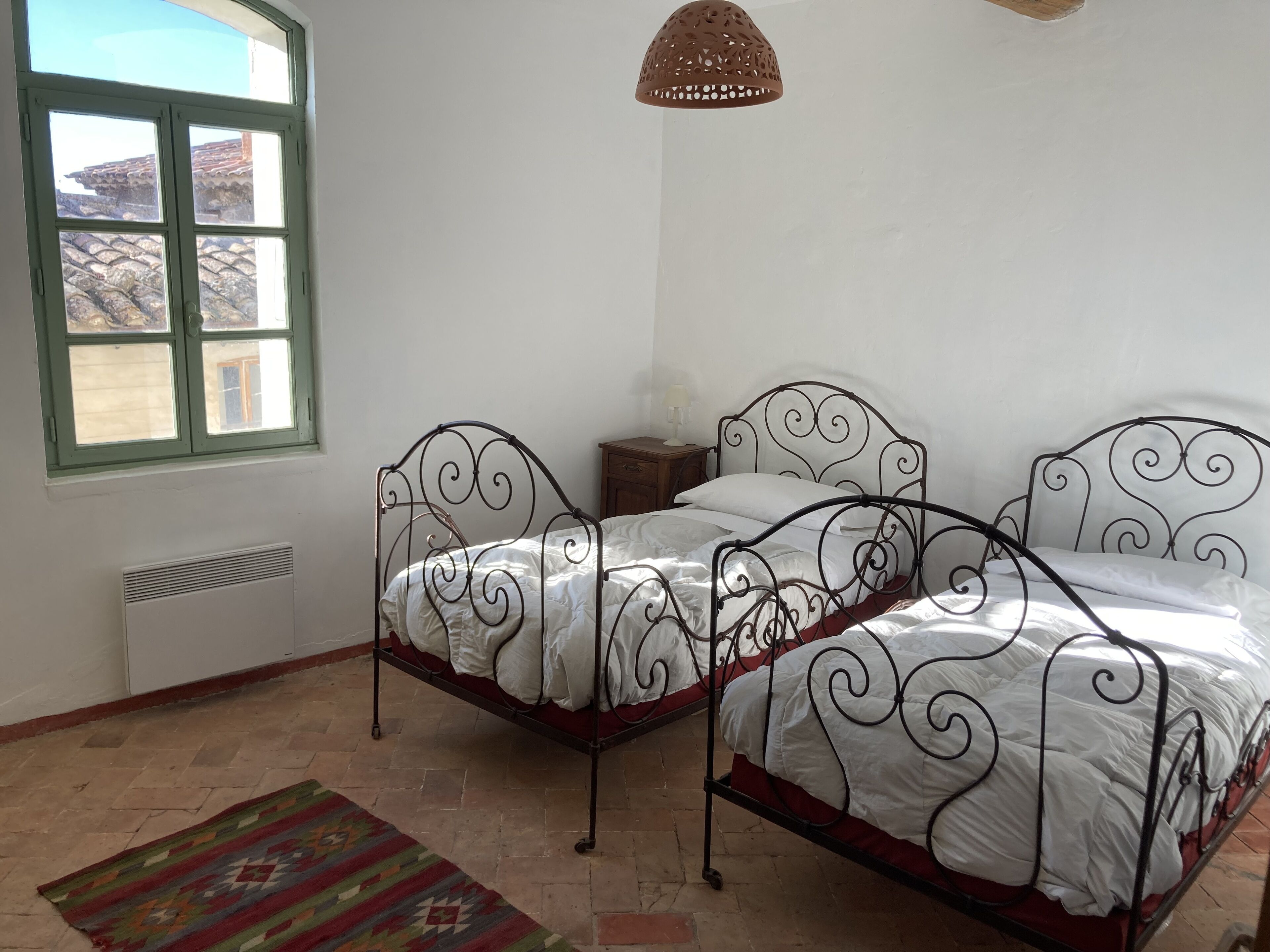 Ein Schlafzimmer mit zwei Metallbetten, einem Fenster, einem Heizkörper und einer Hängelampe.