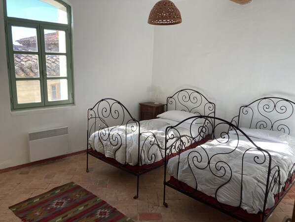 A bedroom with two metal beds, a window, a heater, and a hanging lamp.