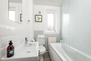A modern bathroom with a white sink, toilet, and bathtub. There is a window with a view of the outside, and a mirror on the wall. - Boase Avenue (No 24) | St Andrews (St Andrews)