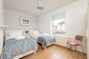 A bedroom with two beds, a window with a view, a chair, and a ceiling light. - Boase Avenue (No 24) | St Andrews (St Andrews)