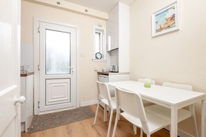 A small, bright room with a white door, a white table with two chairs, a small kitchen area with a sink and a clock on the wall. - Boase Avenue (No 24) | St Andrews (St Andrews)