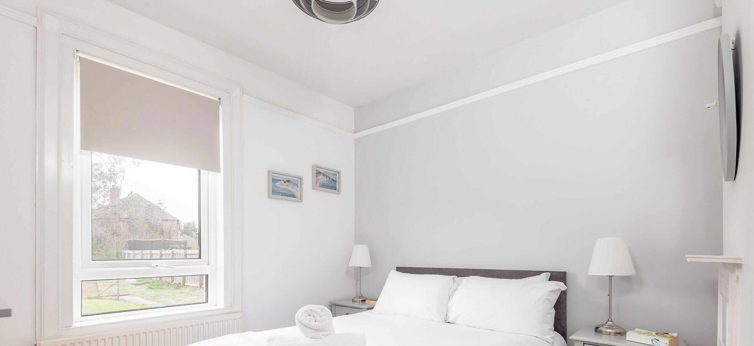 Une chambre à coucher comprenant un lit, deux tables de chevet, une fenêtre et deux cadres photo fixés au mur.