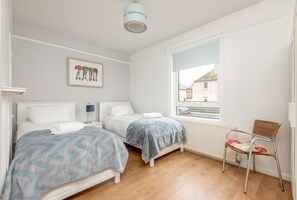 Ein Schlafzimmer mit zwei Betten, einem Fenster mit Blick, einem Sessel und einer Deckenleuchte.