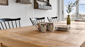 A wooden dining table with chairs, a vase with a plant, and a stack of plates. - 3 bedroom cozy home in Skibby (Skibby)