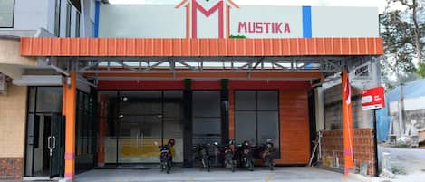 A building with a sign reading "MUSTIKA" and a row of motorcycles parked outside.