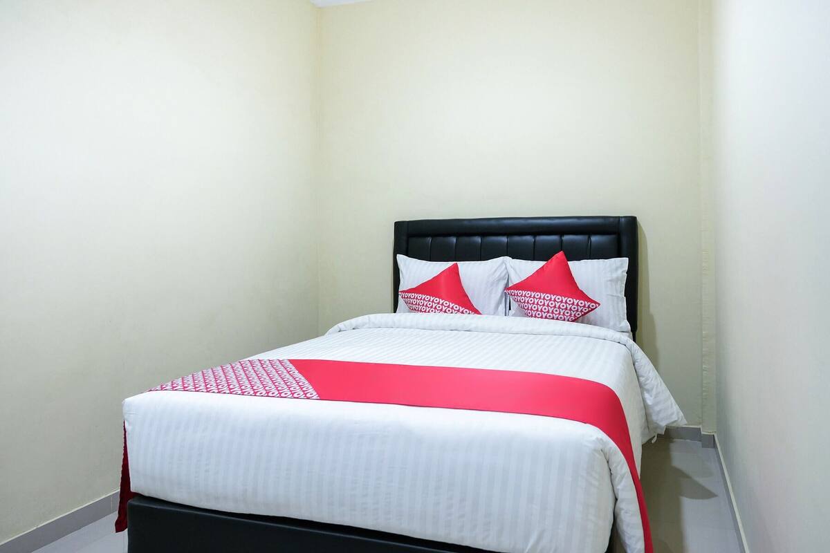 A neatly made bed with a black headboard and white bedding, including a red and white patterned bedspread and matching pillows.
