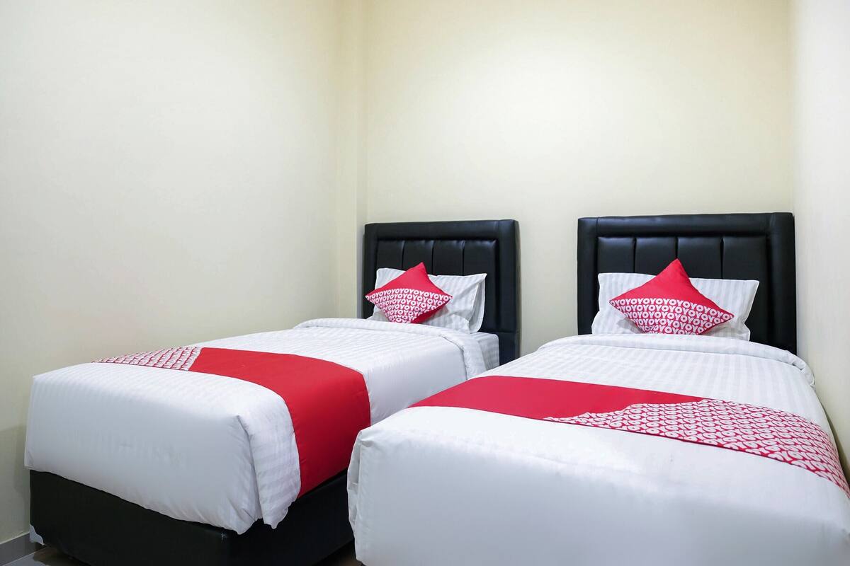 Two single beds with black headboards and white bedding, each with a red pillow.