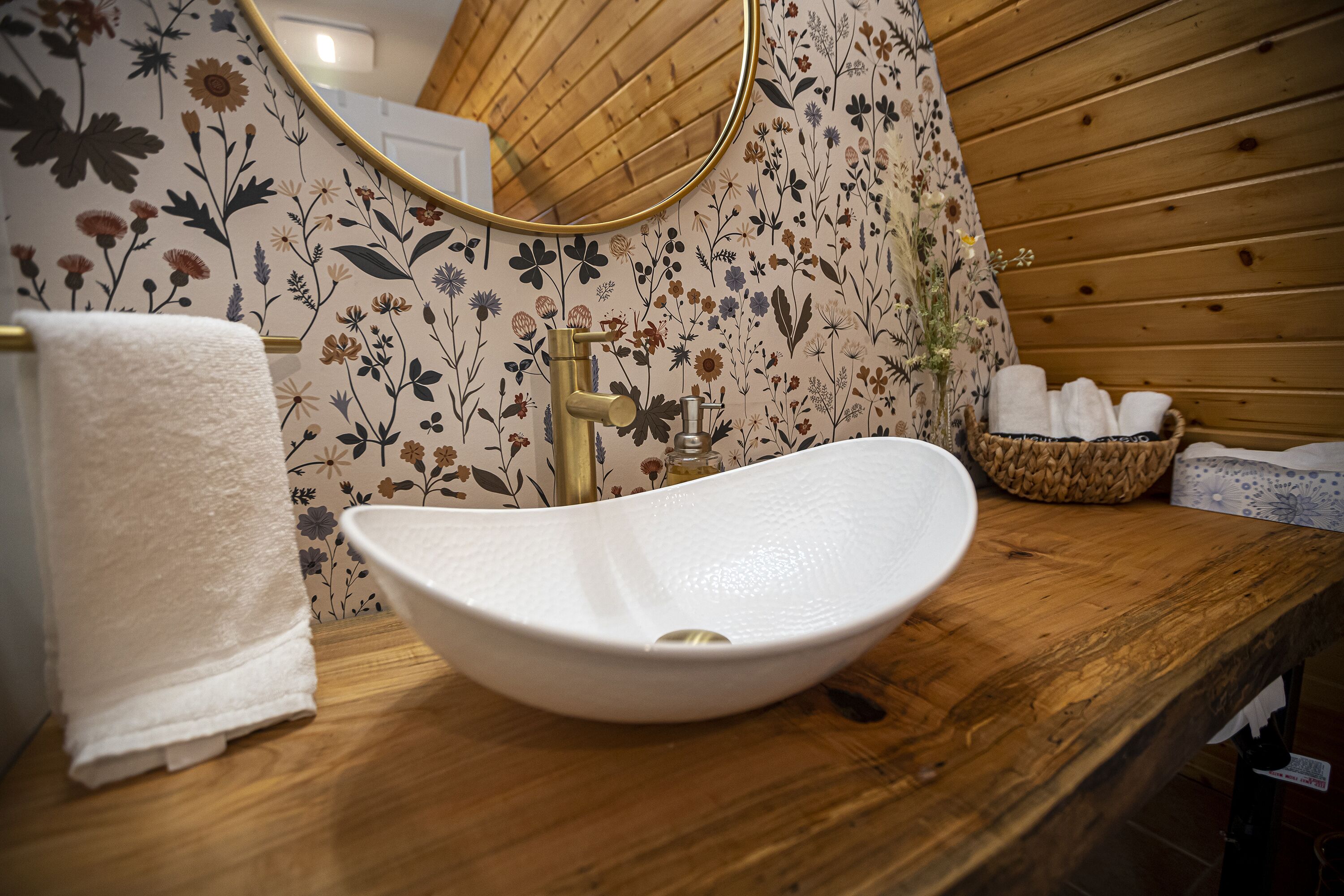 Een houten wastafelmeubel met een witte wasbak, een gouden kraan en een spiegel erboven.