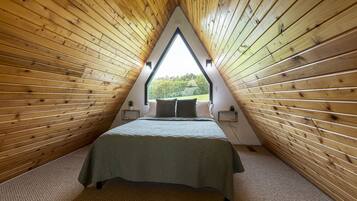 A triangular room with wooden walls and a bed with a green bedspread.