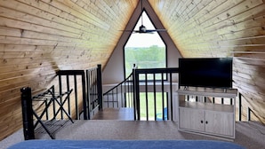 Camera mansardata accogliente con soffitto spiovente, una TV su un mobile in legno e vista su un lago.