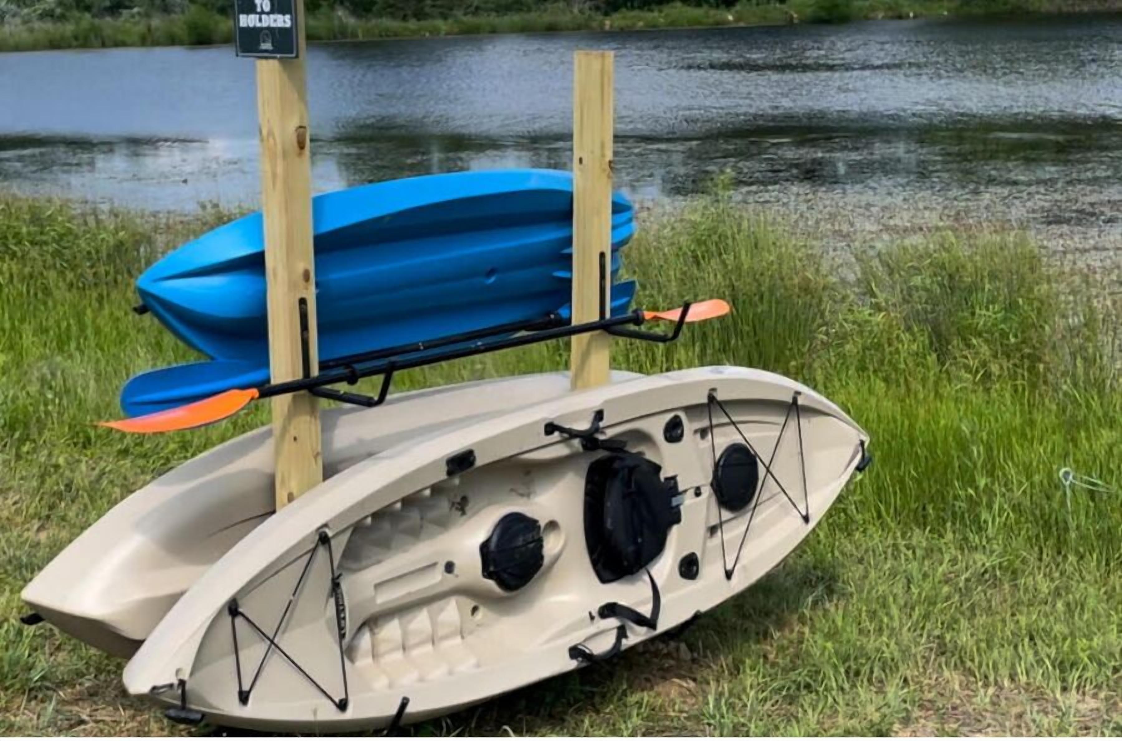 A kayak with a blue storage bag and orange paddle, secured on a stand by a riverbank.