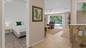 A hotel room with a bed, a desk, a chair, a stone accent wall, and a view of the outdoors. - Heated Pool, 4BR & 3 Full Baths — 10 Min to AMI (Bradenton)