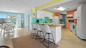 A modern kitchen with white cabinets, a central island with bar stools, and a dining area with a table and chairs. - Heated Pool, 4BR & 3 Full Baths — 10 Min to AMI (Bradenton)