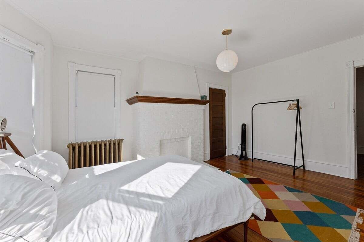 Une chambre à coucher avec un lit, un radiateur, un luminaire suspendu et un tapis coloré.