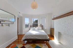 A bedroom with a bed, a mirror, a fireplace, and a window. - Spacious 7BR Beach House with Arcade and Porch! (Wildwood)