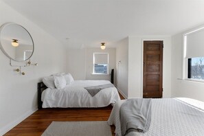 Un dormitorio con dos camas, suelo de madera, un espejo grande y una ventana.