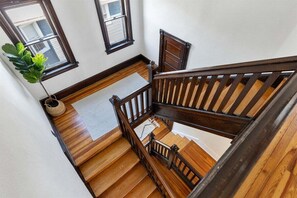 Un escalier en bois avec une rampe, une plante en pot et une fenêtre avec des stores.